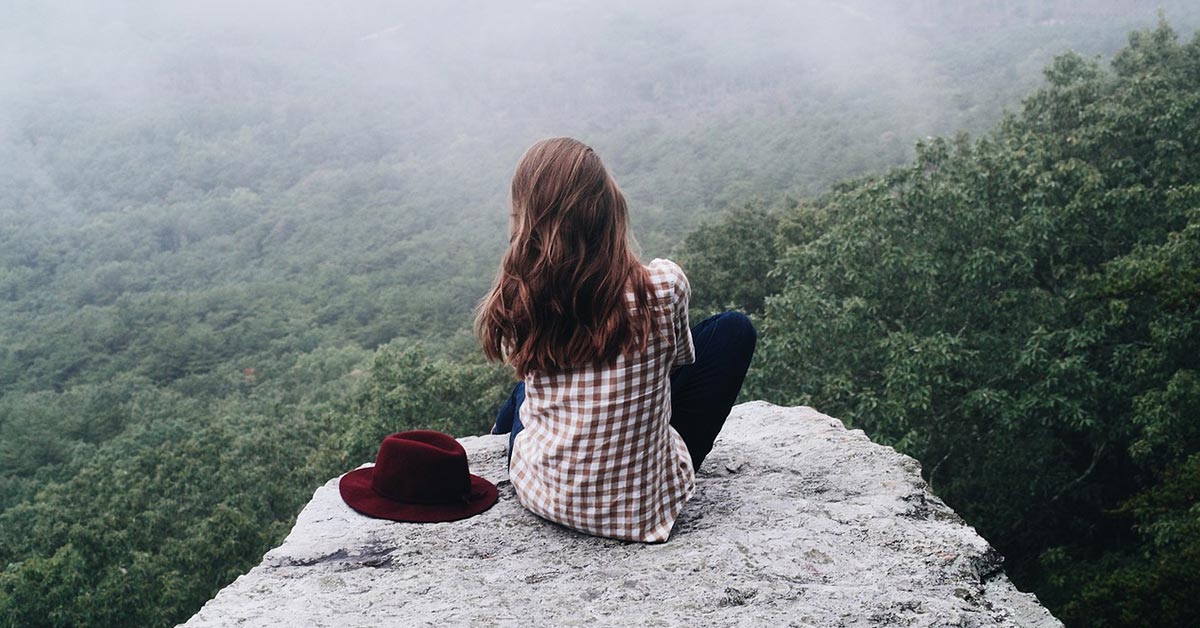 Junge Frau sitzt auf einem Felsen und blickt über die Landschaft