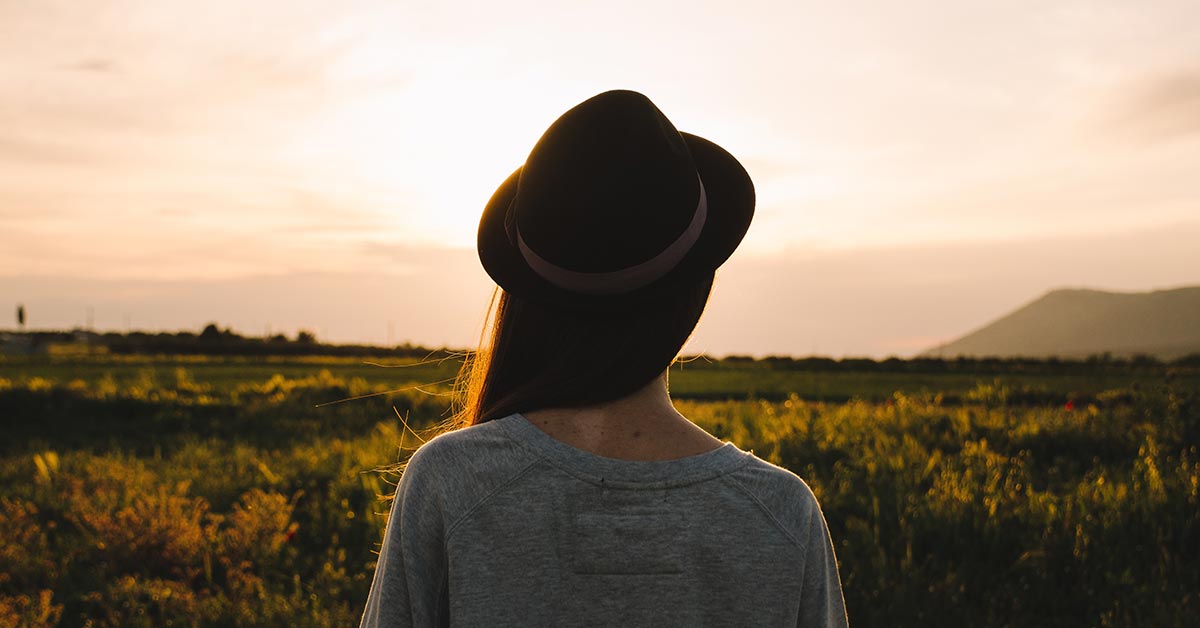 Junge Frau blickt auf eine Wiese bei Sonnenaufgang