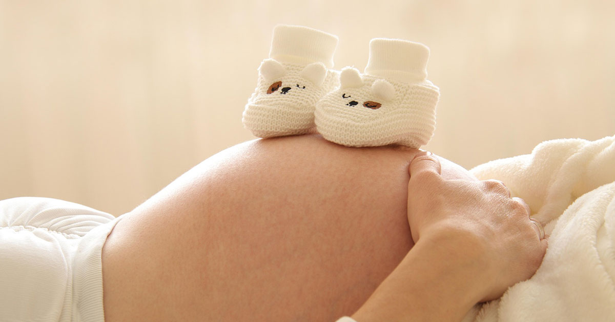 Der Bauch einer Schwangeren mit kleinen Babyschühchen