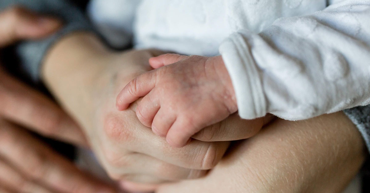 Hände eines Eltern und eines Babys halten sich fest